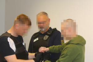 Angeklagtem werden Handfesseln durch Wachtmeister abgenommen.