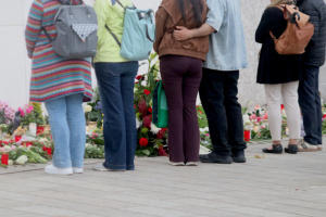 Menschen stehen vor Blumen und Kerzen und halten inne.