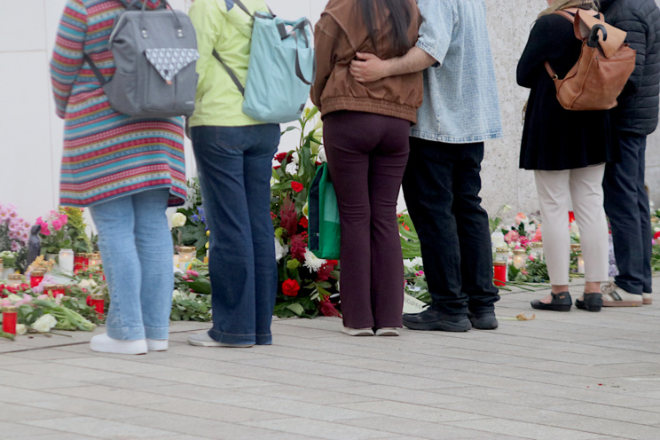 Menschen stehen vor Blumen und Kerzen und halten inne.