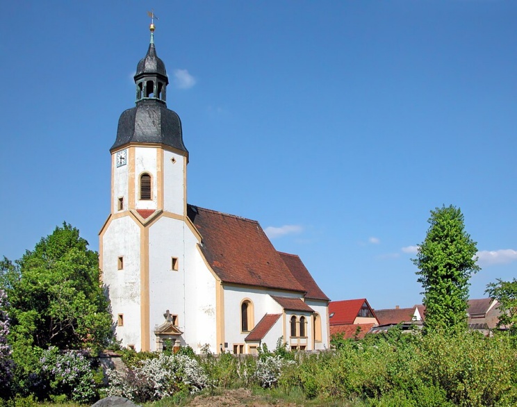 Helles Kirchengebäude vor blauem Himmel.